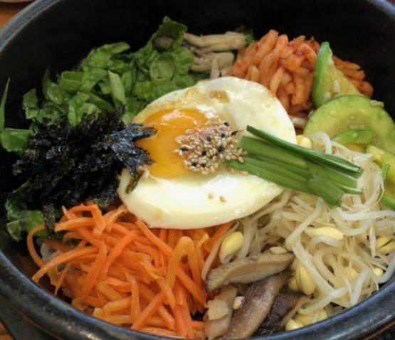 Dolsot bibimbap sizzling in a hot stone pot with a raw egg on top