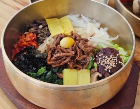 A bowl of bibimbap arranged in the five traditional Korean colors — red, green, yellow, white, and black — with a glossy egg on top