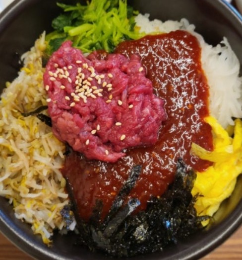 Yukhoe bibimbap topped with raw seasoned beef and an egg yolk
