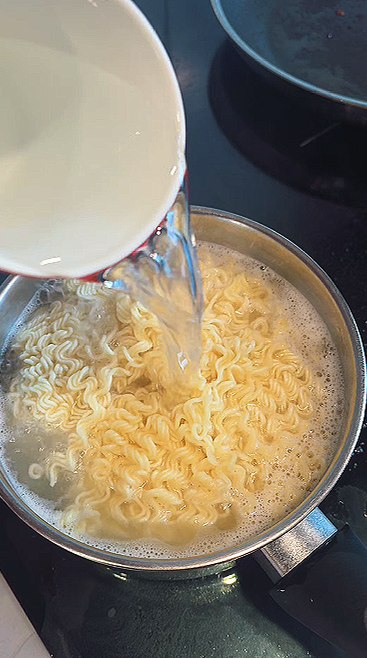 Pouring a cup of cold water into the boiling noodles