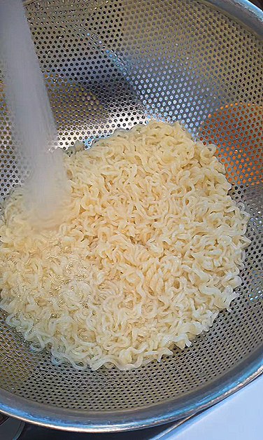 Rinsing the cooked noodles in a strainer under cold water