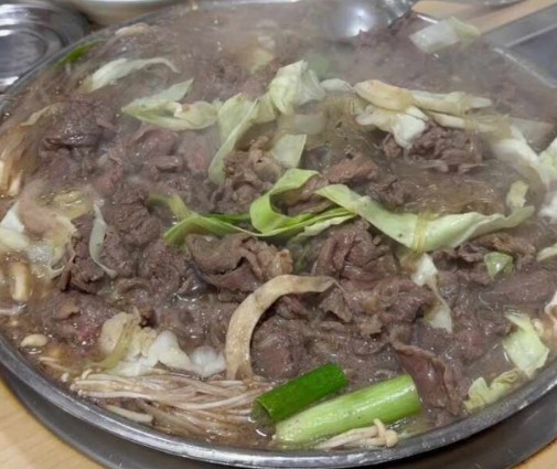 Seoul-style soup bulgogi cooking in a shallow pan with onion, mushroom, and glass noodles