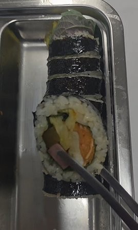 A close-up cross-section of homemade gimbap, showing rice, egg, ham, pickled radish, and carrot inside a seaweed wrap