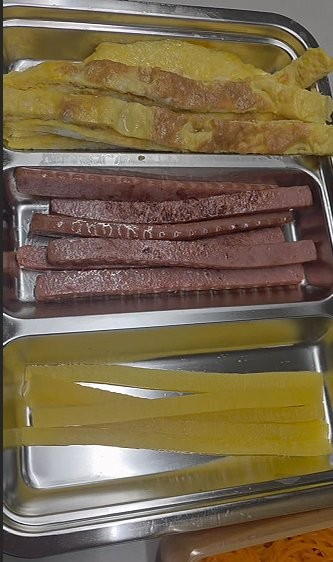 Gimbap fillings prepped in long strips — egg, ham, pickled radish, and carrot