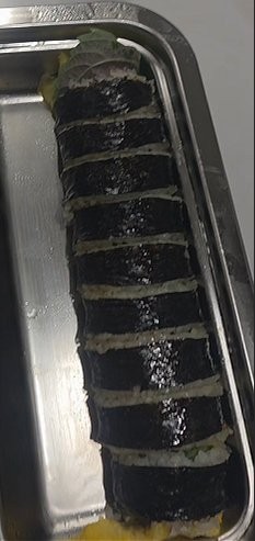 A finished gimbap roll on the bamboo mat before slicing