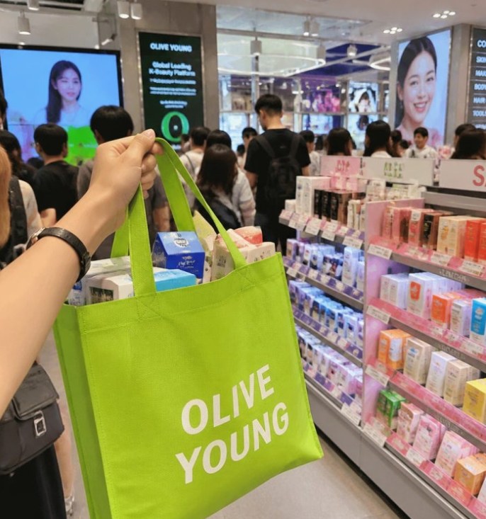 Olive Young shopping bag held inside a busy beauty store.