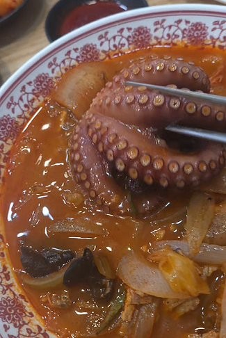 A red bowl of muneo-jjamppong — Korean spicy seafood noodle soup with octopus