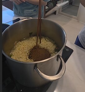 Adding the powder seasoning to the drained noodles in the pot