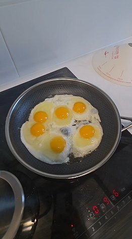 Six fried eggs cooking in a pan on the stove
