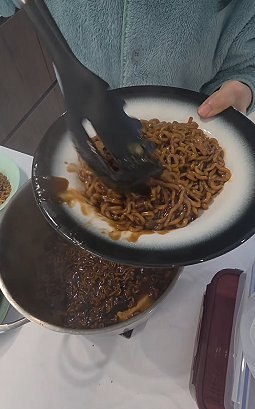 A plate of finished jjapaguri topped with a fried egg, with the pot in the background
