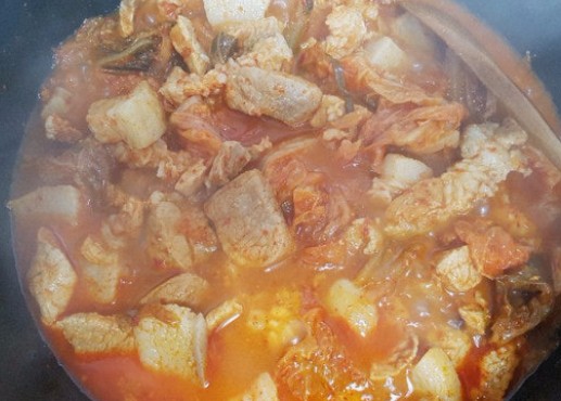 Kimchi jjigae simmering with pork belly and aged sour kimchi in a red broth