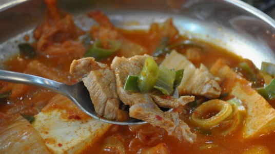 A spoonful of kimchi jjigae over a bowl of white rice