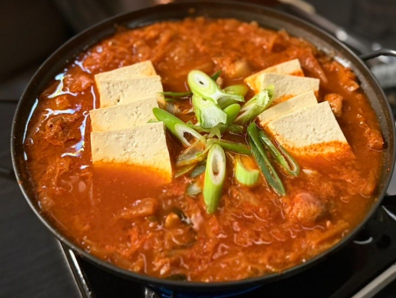 A bubbling ttukbaegi (stone pot) of kimchi jjigae — Korean kimchi stew with pork and tofu