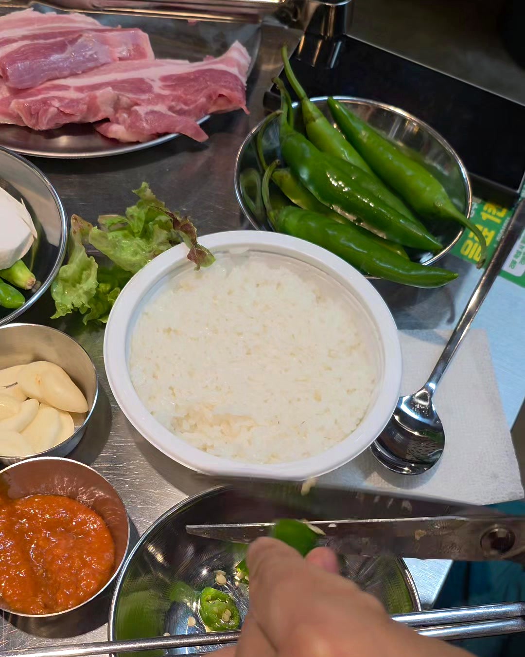 Cutting a fresh cheongyang green chili to add to a samgyeopsal ssam at a Korean BBQ table