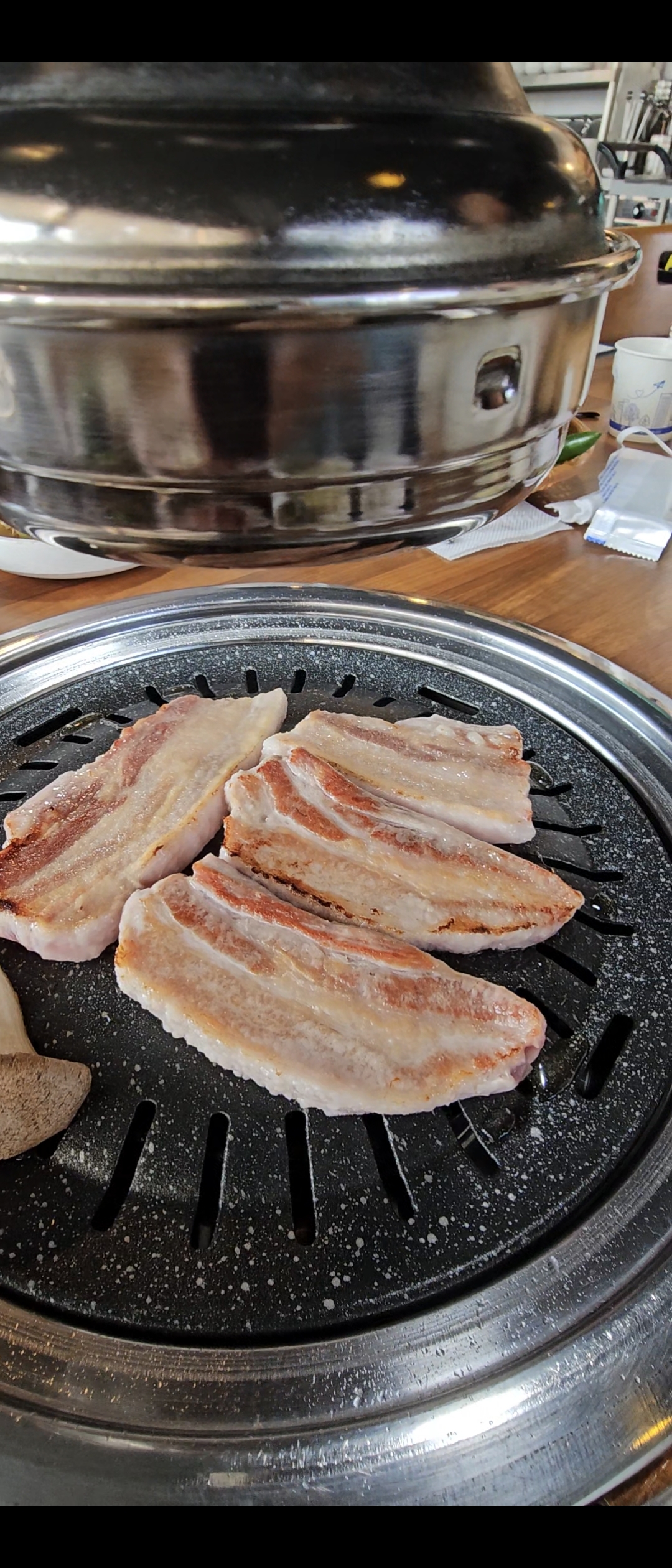 Samgyeopsal searing on a round Korean BBQ grill, edges turning golden-brown