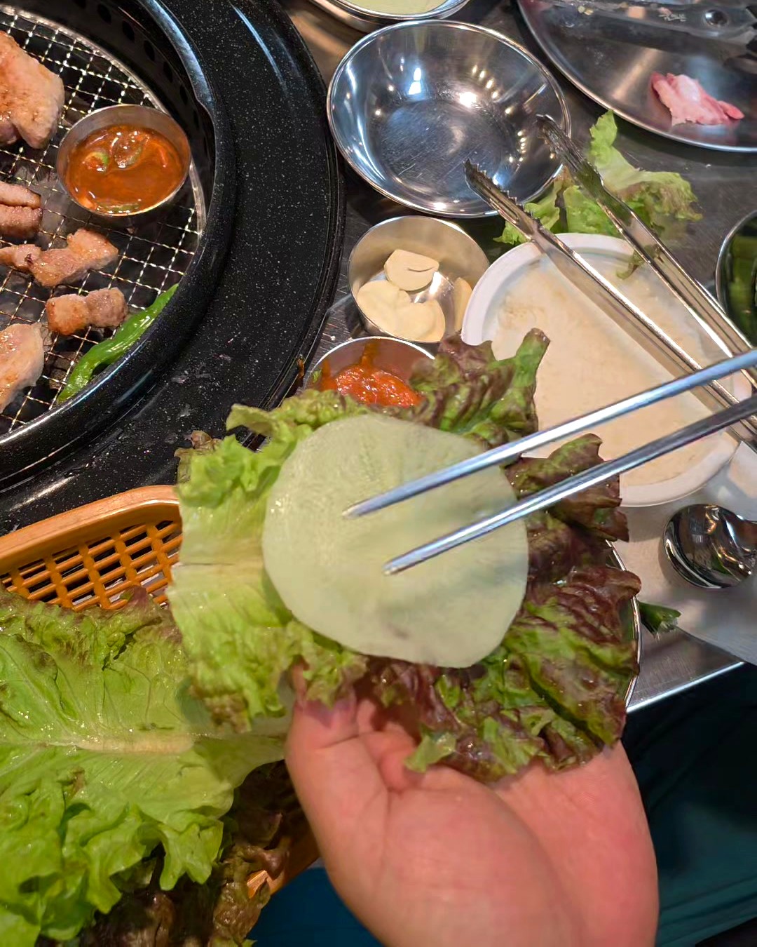 A thin ssammu pickled-radish sheet laid on a lettuce leaf for wrapping Korean BBQ pork belly
