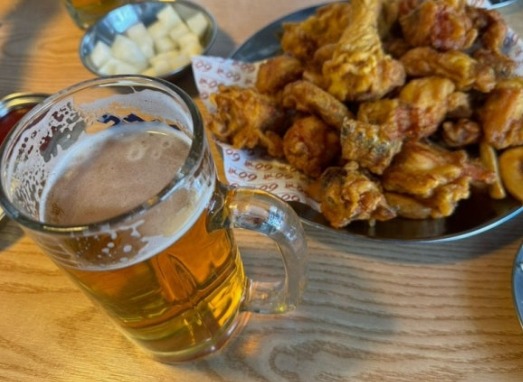A mug of draft beer beside a plate of Korean fried chicken with pickled radish
