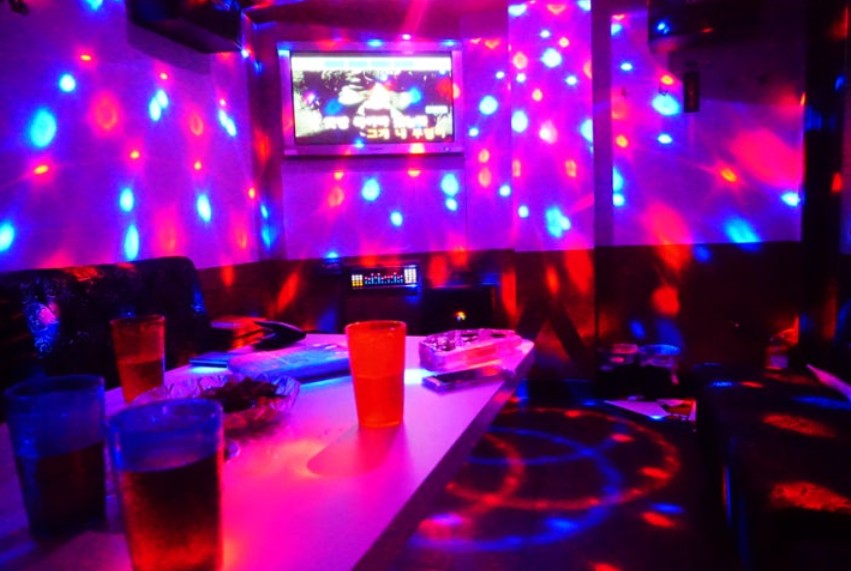 Inside a Korean noraebang — a private karaoke room with sofa, mics, screen, and disco lighting