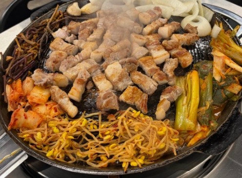 Samgyeopsal grill loaded with pork alongside kimchi, garlic, and mushrooms sizzling on the side
