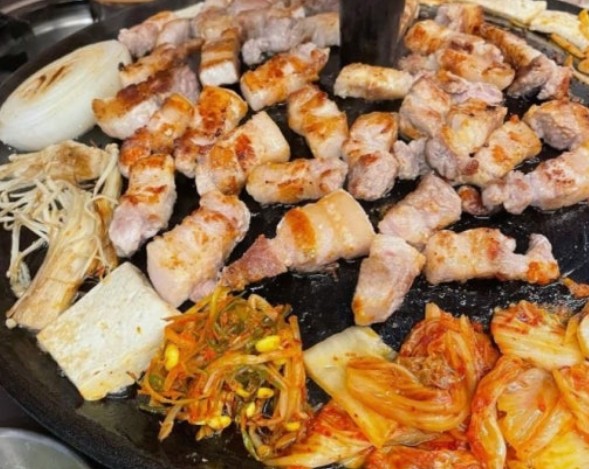 Thick strips of samgyeopsal (Korean pork belly) sizzling on a tabletop grill