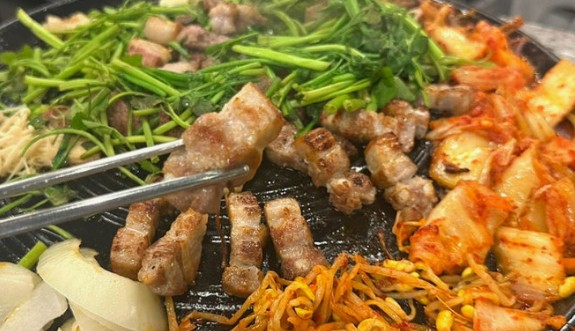 A Korean BBQ tabletop with samgyeopsal, tongs, banchan, and shots of soju