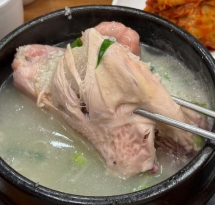 A whole samgyetang chicken split open to show the glutinous rice stuffing inside