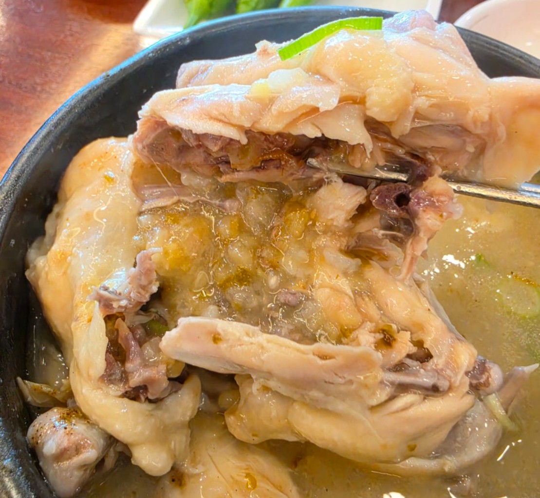 The samgyetang chicken opened up with a spoon, showing the softened glutinous rice and garlic packed inside the cavity