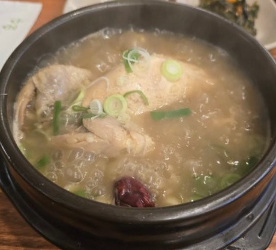 Samgyetang broth with jujube, garlic, and ginseng around a whole young chicken