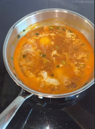 An egg cracked into the simmering Samyang ramen broth in the empty pot