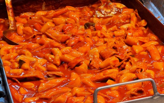 A wide iron pan of tteokbokki simmering with fish cakes and boiled eggs at a street stall